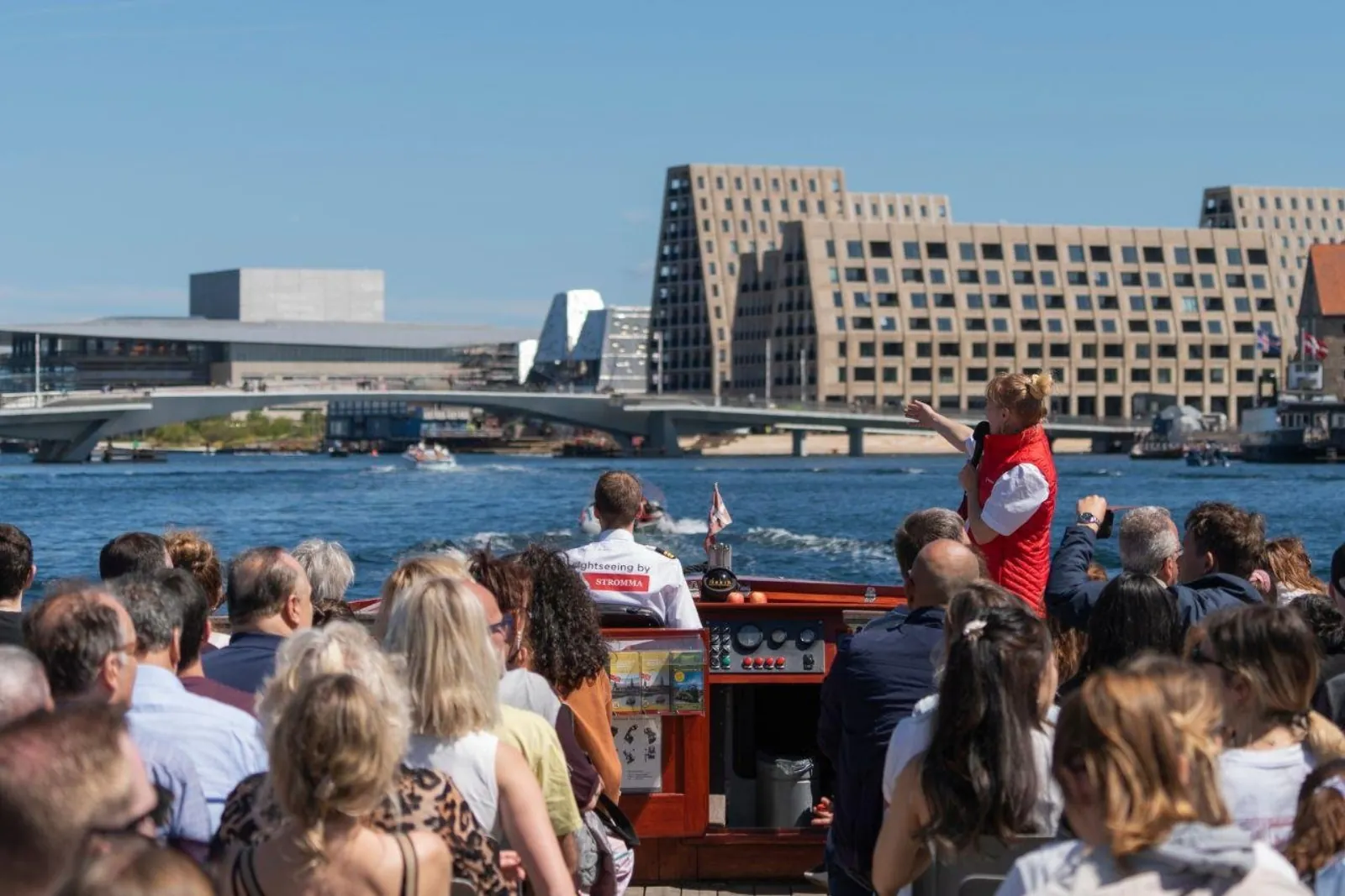 Passengers on deck looking across the harbour at modern waterfront architecture