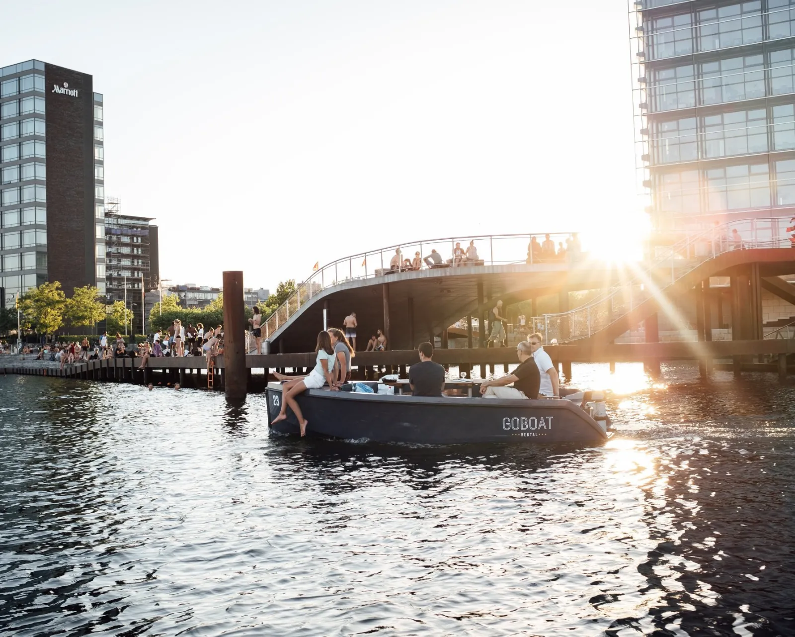A GoBoat on the harbour with the sun behind a modern bridge