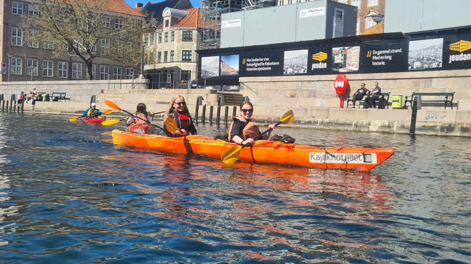 A group of kayakers in orange kayaks on the harbour