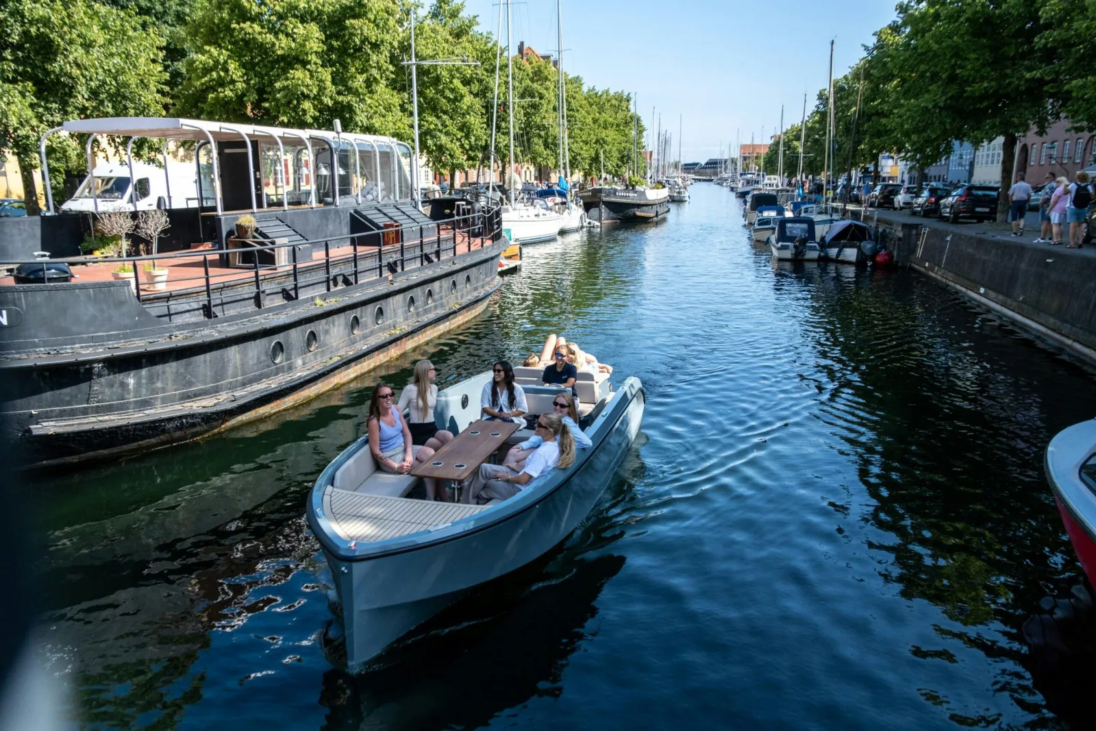 A GoBoat full of guests in a quiet canal lined with moored boats