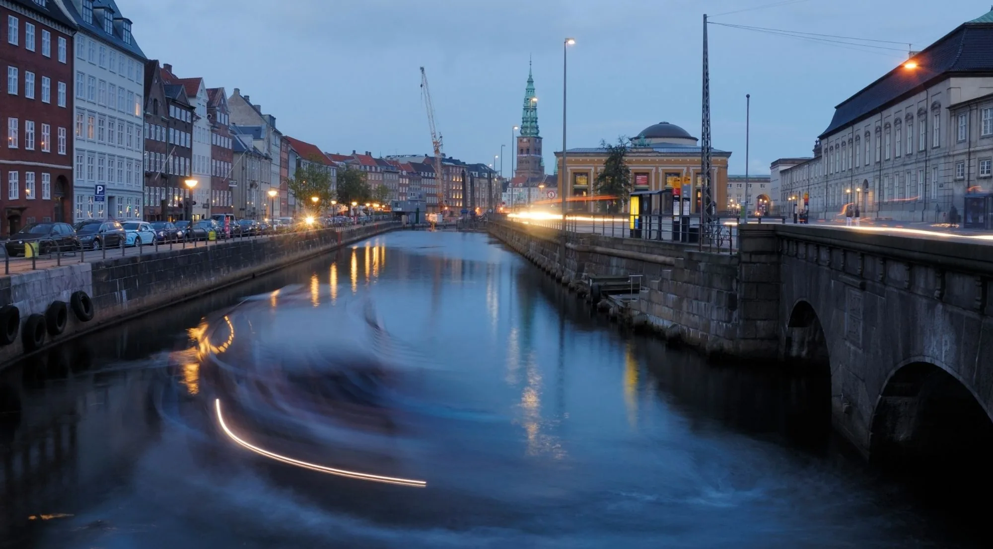 A canal by Gammel Strand at dusk with a spire and boat light trails