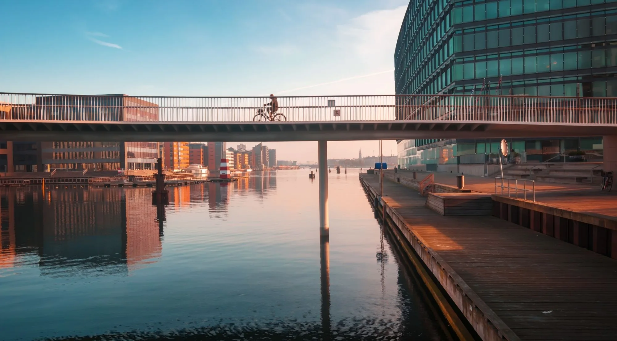 A cyclist crossing a harbour footbridge at sunrise