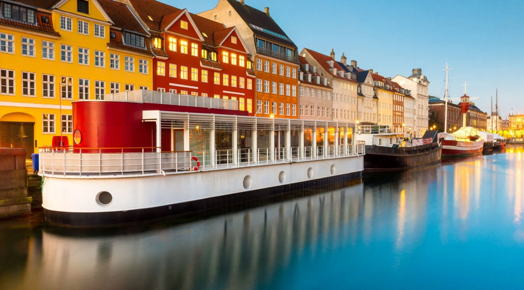 A moored white boat reflected in the water at Nyhavn in the blue hour